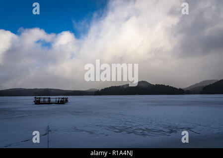Beautiful winter landscape on a frozen lake in Rhodope Mountains - sunset over cracked ice, wooden raft stack im the middle Stock Photo