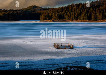 Beautiful winter landscape on a frozen lake in Rhodope Mountains - sunset over cracked ice, wooden raft stack im the middle Stock Photo