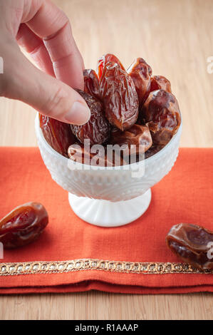 A person's hand taking a dried organic date from a bowl on a brightly colored orange cloth. Stock Photo