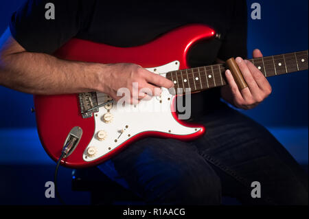 A close up view of a man playing a red and white electric guitar. Stock Photo