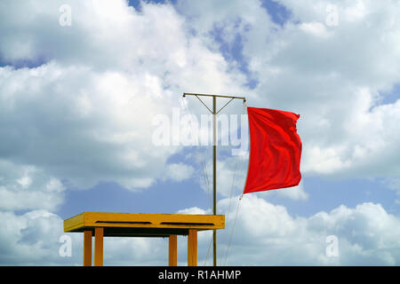Red flag next to a lifeguard chair at the beach. Swimming in the sea is not allowed. Stock Photo