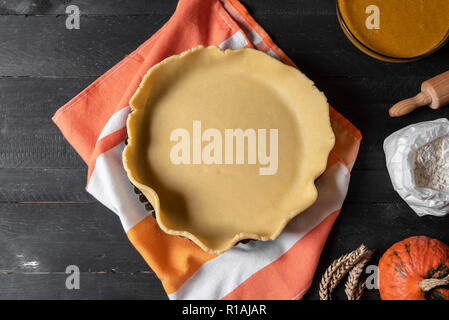 Cooking pumpkin pie concept with the pie dough in a  baking tray, pumpkin pie filling, flour and pumpkin on the side, on rustic table. Above view. Stock Photo