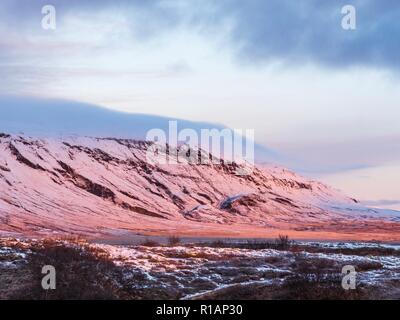 Pink glow of sunrise on the side of a snow covered mountain in central Iceland Stock Photo