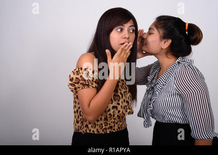 Studio shot of young fat Persian teenage girl whispering to youn Stock Photo