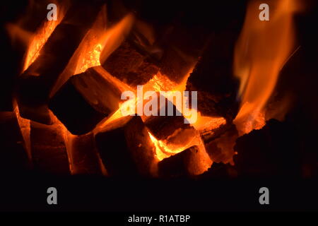 Close up of Brown Coal Briquettes on fire with red yellow flames inside a special solid furnace, red and orange blurry texture on a black background. Stock Photo