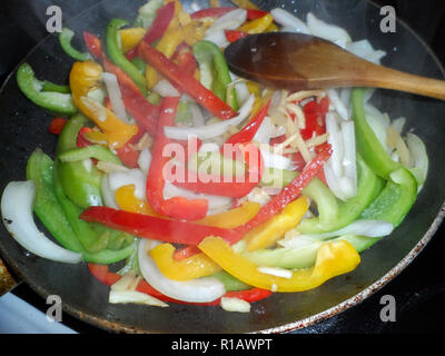 Sliced Red, Green and Yellow bell peppers being stir fried in a shallow frying pan Stock Photo