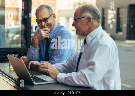 Senior businessmen at cafe with laptop discussing work and smiling. Senior business professionals having casual discussing over work at cafe after wor Stock Photo