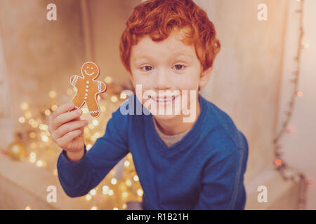 Smiling red-haired boy showing gingerbread man Stock Photo