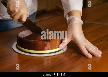 Prague mousse cake. Woman cuts off slice of cake with a kitchen knife. Cooking in a pastry shop. Stock Photo