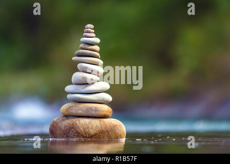 Close-up abstract image of wet rough natural brown uneven different sizes and forms stones balanced like pyramid pile landmark in shallow water on blu Stock Photo