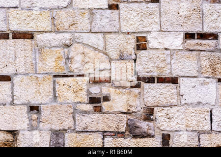 Fragment of the old wall of their beige stone with inclusion of red brick for use as a background. Stock Photo