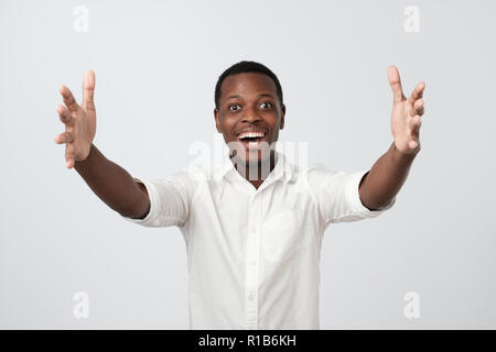 Free hugs for person who had bad day. Cheerfull african man in white shirt, pulling hands towards camera, wanting to cuddle, smiling broadly, welcomin Stock Photo