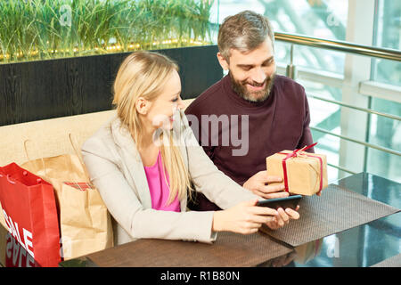 Portrait of adult couple exchanging presents while sitting at table in shopping mall cafe, copy space Stock Photo