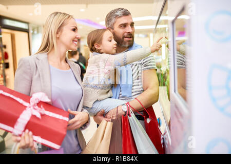 Girl with parents exploring shop window in mall  Stock Photo