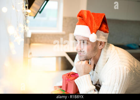 Dreamy man in Santa hat looking away Stock Photo