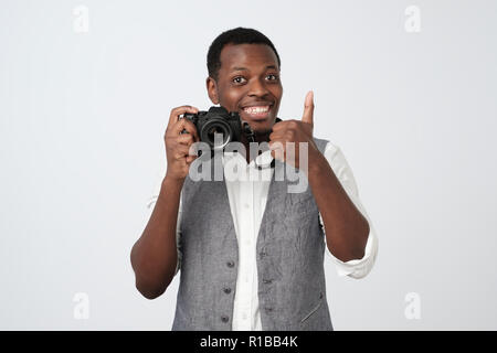 African handsome man holding photo camera and smiling, showing thumb up. Hobby concept. Stock Photo