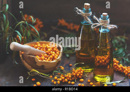 Natural, organic sea-buckthorn berry in bowl and sea buckthorn oil in glass vintage bottle on dark wooden background. Dark rustic style, natural remed Stock Photo