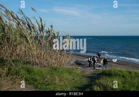 Police officers seen inspecting the dinghy after arriving on the beach with a group of migrants. A dinghy with migrants and two dead arrived at the Chilches beach near the coast of Velez Málaga, in Malaga. According to the media and witnesses, some of the migrants from Morocco escaped at the beach while the two corpses were found inside the small boat. Stock Photo