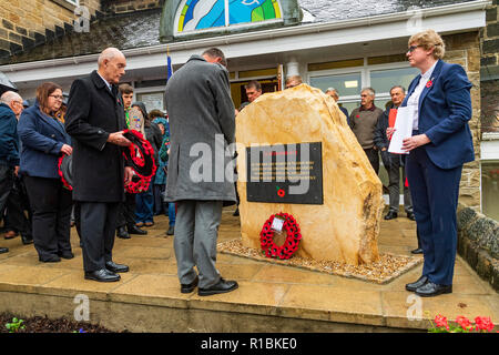 Yeadon, Leeds, West Yorkshire, UK 11th November, 2018. People are gathered round the new war memorial stone in front of Yeadon Methodist Church for a service of dedication & remembrance. The first poppy wreath has been laid and a man is bowing his head in respect. Ian Lamond/Alamy Live News. Stock Photo