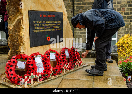 Yeadon, Leeds, West Yorkshire, UK 11th November, 2018. Close-up of the plaque inscription & crosses & poppy wreaths laid at the base of the new war memorial stone in front of Yeadon Methodist Church, on the anniversary of the end of the First World War. A man is bending down placing a cross in the ground. Ian Lamond/Alamy Live News. Stock Photo