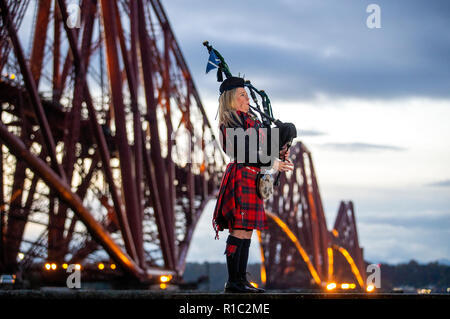 Piper Louise Marshall, wearing a special commemorative red tartan, plays Battle's O'er, the traditional Scottish lament played at the end of battle, at dawn alongside the Forth Bridge at North Queensferry on the 100th anniversary of the signing of the Armistice which marked the end of the First World War. Stock Photo