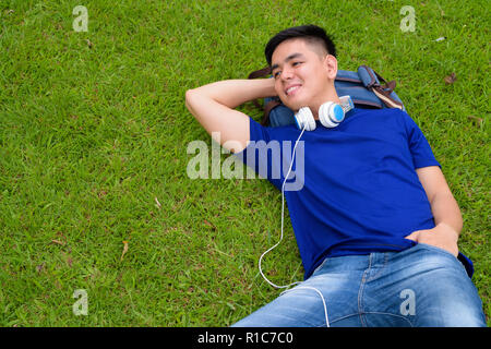 Young handsome Asian man relaxing at the park with headphones Stock Photo