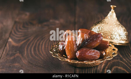 Metal plate of sweet organic dates on dark wooden table. Dried dates with copy space for text. Banner. Stock Photo