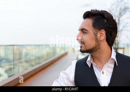 Profile view of young handsome Indian man thinking at rooftop re Stock Photo