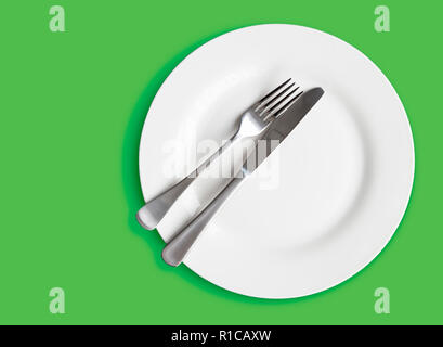 Knife and fork on white plate isolated on green background - top view photo Stock Photo