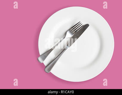 Knife and fork on white plate on pink background - top view photo Stock Photo