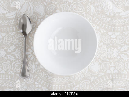 Bowl and silver spoon empty on patterned table cloth - Top view photo Stock Photo