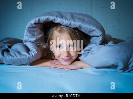 Smiling and cheerful sweet small girl looking happy lying in bed at night or morning feeling joy and rest in Sleeping Comfort Happy Family and Childre