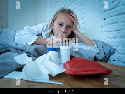 Sweet sick cute girl feeling sick lying in bed with medicines thermometer hot water bag suffering from Cold and Winter Flu Virus Sneezing Running Nose Stock Photo
