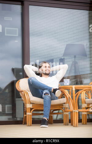 Positive millennial man sitting on outdoors armchair at home Stock Photo