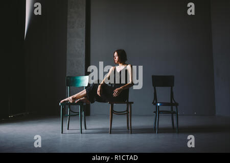 The social theme female loneliness pain suffering. Abastration male violence family. A young beautiful Caucasian woman in black clothes sitting on thr Stock Photo