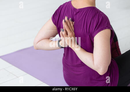 People, sport, yoga and healthcare concept - Middle-aged woman sitting on yoga mat with hands behind her back Stock Photo