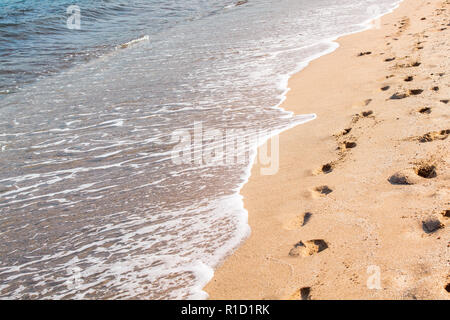 waves striking the beach and footprints in the sand Stock Photo