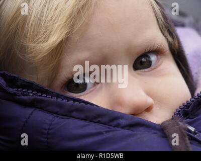 Blond caucasian baby girl with gray eyes in winter jacket looking at camera Stock Photo