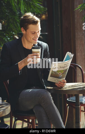 A businessman portrait, he sits at a cafe having a cup of coffee reading a newspaper. A successful young entrepreneur portrait. Stock Photo