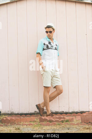 A handsome male model posing in Summer Clothes outdoor standing against a plain wooden wall. Stock Photo