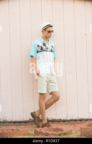 A handsome male model posing in Summer Clothes outdoor standing against a plain wooden wall. Stock Photo