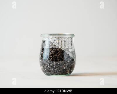 Healthy breakfast concept and idea - two colors chia pudding on white tabletop. Glass jar with black charcoal and white vegan milk chia pudding. Copy space for text Stock Photo