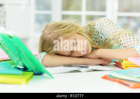 Tired schoolgirl sleeping at desk after studying Stock Photo