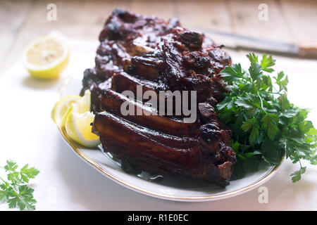 Appetizing baked glazed veal or pork ribs served with lemon and herbs. Selective focus. Stock Photo