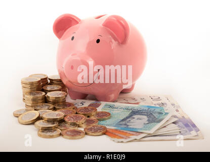 Pink Piggy bank on lots of pound notes and pound coins Stock Photo