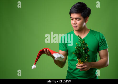 Young handsome Filipino man ready for Christmas against green ba Stock Photo