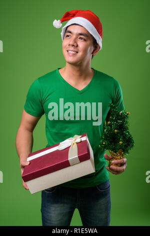 Young handsome Filipino man ready for Christmas against green ba Stock Photo