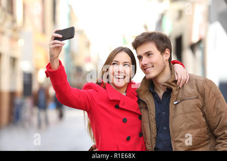 Happy couple taking selfies with a smart phone in the street in winter Stock Photo