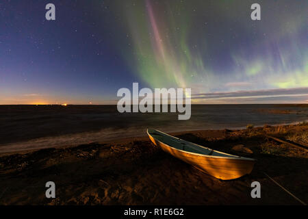 Northern lights and moonlight illuminates the rowing boat on beach Stock Photo