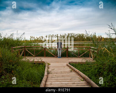 A person in a viewpoint with a wooden railing contemplating a river in autumn Stock Photo